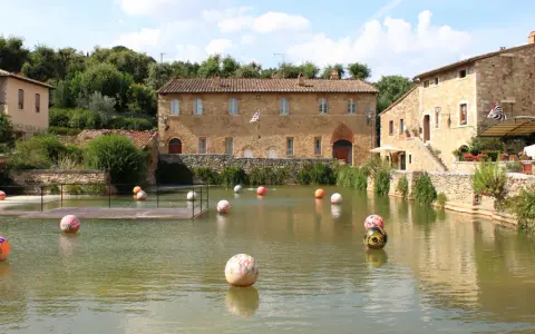 Paesini puglia con un laghetto pieno di sfere colorate, circondato da antichi edifici in pietra e vegetazione rigogliosa.