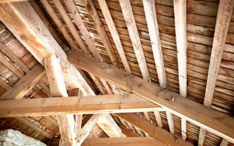 Vue rapprochée d'une charpente ancienne en bois, témoignant d'un savoir-faire artisanal. Un futur projet de traiter charpente pour la préserver.
