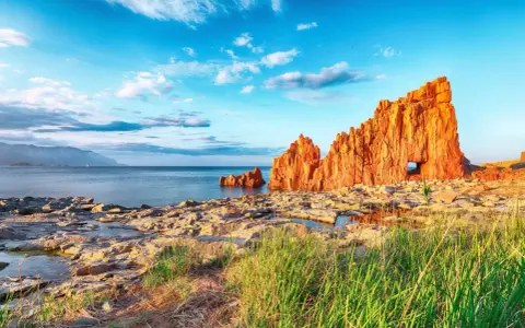 Scogliere rosse a picco sul mare blu, con un arco naturale, vicino ad Arbatax centro storico.