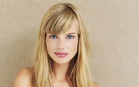 Blonde Frau mit blauen Augen und Pony. Eine Anleitung zum Pony schneiden könnte hier nützlich sein, um diesen Look zu erzielen.