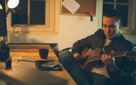 Mężczyzna gra na gitarze, ćwicząc skale gitarowe przy biurku.