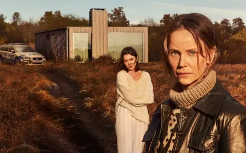 Två kvinnor står i ett torrt landskap framför ett modernt hus. En polisbil syns i bakgrunden. Sanningen serie.