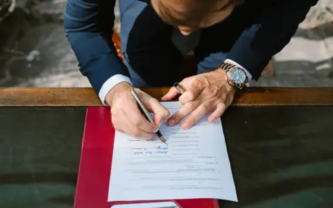 Mężczyzna w garniturze podpisuje dokument. Zastanawia się, jakim nazwiskiem podpisać się na ślubie cywilnym, wybierając to właściwe.