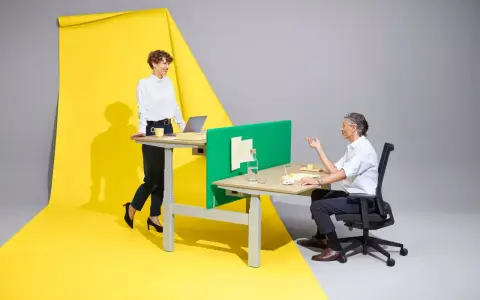 Femme en position debout statique, souriante, devant un bureau. Homme assis à un bureau, discutant. Fond jaune et gris.