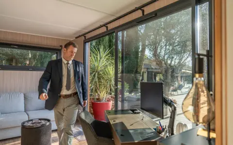 Un homme en costume entre dans un bureau lumineux avec vue sur un jardin. C'est la définition du home office : travailler depuis chez soi.