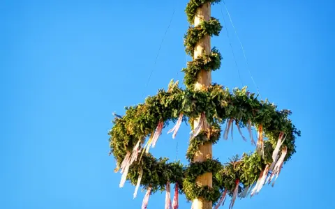 En midsommarstång, dekorerad med grönt och band, mot en klarblå himmel. Dess midsommarstång betydelse symboliserar sommarsolståndet och fruktbarhet.