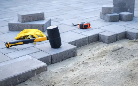Beton pod kostkę czeka na ułożenie. Młotek gumowy, rękawice i miarka gotowe do pracy.