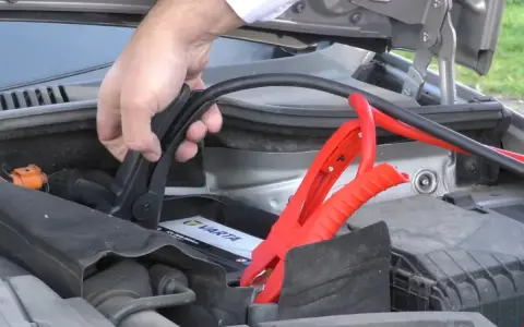 Mano conectando pinzas rojas a la batería de un coche para arrancar con pinzas.