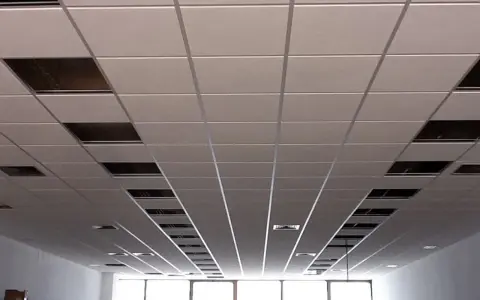 Instalación de un falso techo modular con paneles blancos y perfiles metálicos. Se aprecian huecos para iluminación o ventilación.