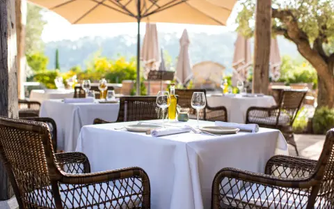 Tables dressées en terrasse, sous un parasol, invitant à savourer une cuisine du terroir authentique. Vins, verres et couverts attendent les convives.