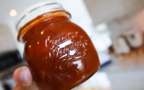 En hand håller ett glas med söt och syrlig rabarberchutney.