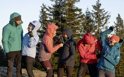 Sechs Personen in bunten Hardshelljacken stehen vor Bäumen. Eine Hardshelljacke schützt vor Wind und Wetter.