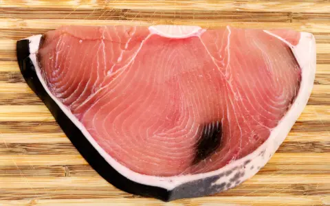 Fetta di tonnina, un pregiato pesce azzurro, su tagliere di legno. La sua carne rosa vivo mostra le tipiche striature.