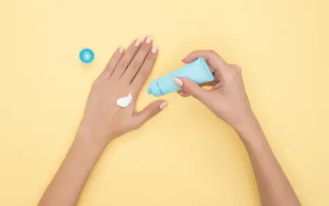 Hände mit Creme, die Glycerin enthält, auf gelbem Hintergrund.