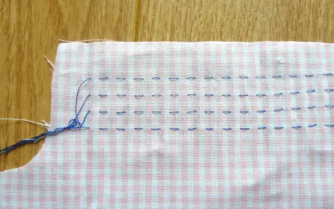 Tissu à carreaux rose et blanc avec des points de couture bleus, préparant un smock couture.