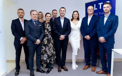 Grupa osób w garniturach i sukience pozuje do zdjęcia na tle banera.