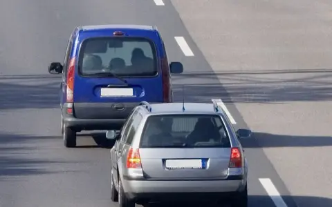 Un veicolo che precede, una monovolume blu, è seguito da un'auto station wagon argentata su una strada asfaltata con segnaletica bianca.