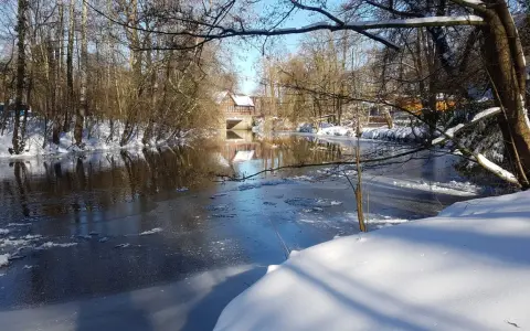 Winterliche Idylle an der **Planwiese Telgte**: Eisiger Fluss, schneebedeckte Ufer und ein Fachwerkhaus spiegeln sich im Wasser.