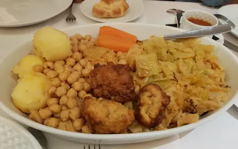 Un plato generoso de cocido madrileño con garbanzos, patatas, zanahoria, repollo y trozos de carne frita.