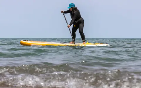 Frau auf einem gelben Stand Up Paddle Board im Meer, mit Paddel in der Hand.