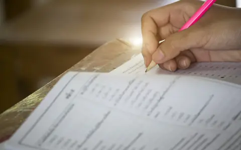Dłoń pisząca ołówkiem po karcie testowej z zaznaczonymi odpowiedziami.
