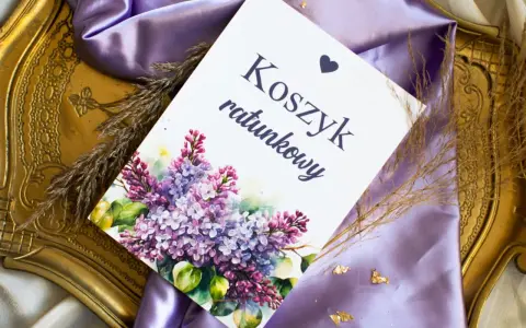 Eleganckie elementy zaproszenia: kartka z napisem "Koszyk ratunkowy", ozdobiona bukietem bzu, na tle fioletowej satyny i złotej ramki.