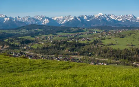 Widok na Tatry z zielonych wzgórz. W oddali widać zabudowania, które mogą być częścią trasy, ile km z Zakopanego do Bukowiny Tatrzańskiej.