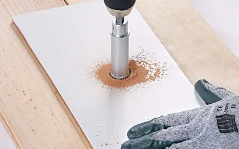 Une perceuse avec une couronne diamantée réalise une découpe carrelage, créant un nuage de poussière fine sur une plaque blanche.