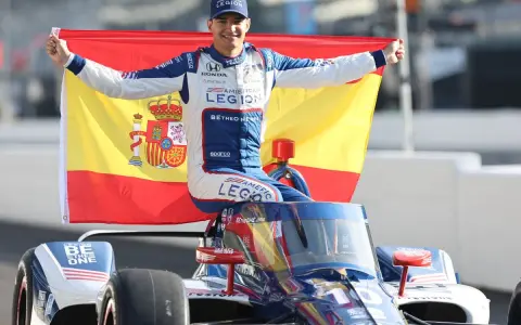 Alex Palou celebra su victoria en las 500 millas de Indianápolis, ondeando la bandera de España sobre su coche de carreras.