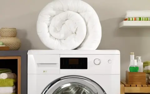 Piumone bianco arrotolato sopra una lavatrice. Pronto per essere lavato in lavatrice a 40 gradi per un bucato fresco e pulito.