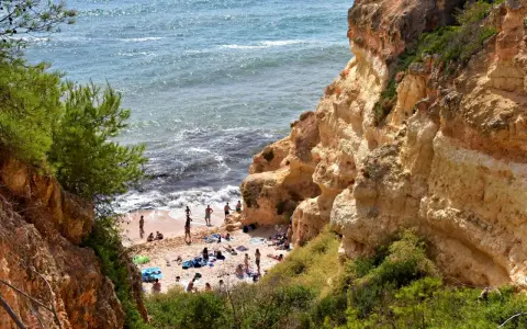 Sonnige Praia do Carvalho mit Felsen, grüner Vegetation und Badegästen am Meer.