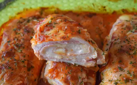 Pechugas de pollo rellenas de queso y jamón, cubiertas con salsa de tomate y queso gratinado, espolvoreadas con perejil fresco.