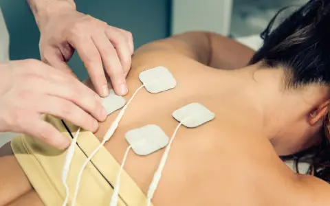Rehabilitacja TENS: na czym polega? Fizjoterapeuta umieszcza elektrody na plecach pacjentki, co jest częścią terapii prądami TENS.