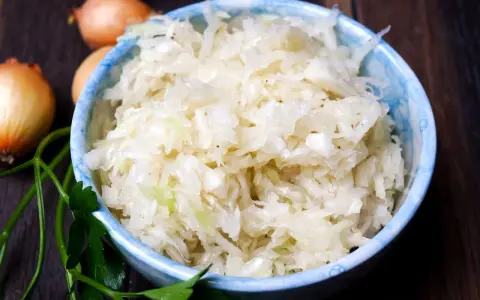 Schüssel mit weltbestem Krautsalat, daneben Zwiebeln und Petersilie. Frisch, knackig und voller Geschmack!