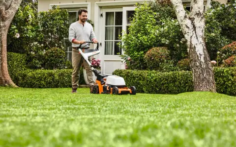 Homme tondant une pelouse verte avec une tondeuse STIHL orange et blanche.