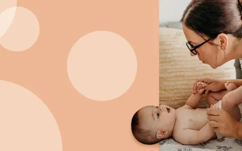 Mama z okularami delikatnie podnosi nóżki dziecka, przygotowując się do zakładania pampersa na stojąco.