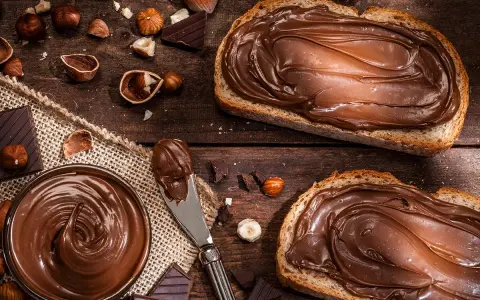 Selbstgemachte Haselnusscreme auf Brot, umgeben von Nüssen und Schokolade. Ein Genuss, der zum Nachmachen einlädt.