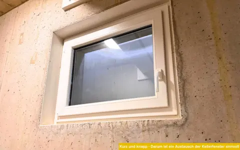 Ein neues, weißes Kellerfenster ist in eine Betonwand eingesetzt. Der Austausch des Kellerfensters verbessert die Dämmung und Sicherheit.