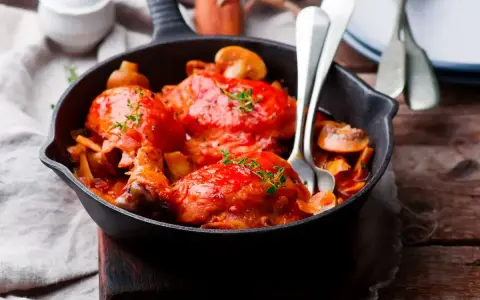 Pollo alla Marengo succulento in padella con funghi e pomodoro, guarnito con timo fresco.
