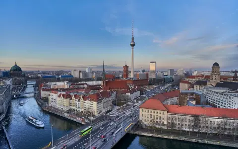 Ampio panorama berlino con la Torre della Televisione, il Duomo e il fiume Sprea. Traffico e barche animano la scena urbana.