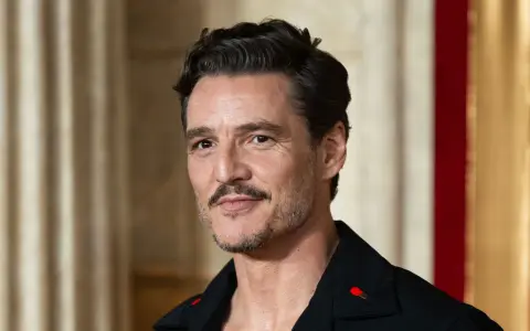 Pedro Pascal con cortes de pelo hombre corto por los lados y largo arriba, luciendo un pin de cerilla en su solapa.