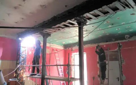 Trabajadores realizan el apeo de muro de carga con soportes metálicos y soldadura. El techo está en proceso de demolición.
