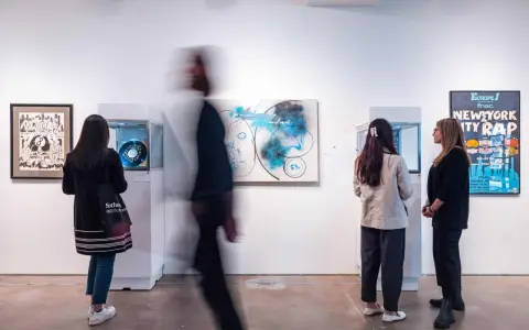 Visitors observe abstract art and a "New York City Rap" poster at a gallery exhibition.