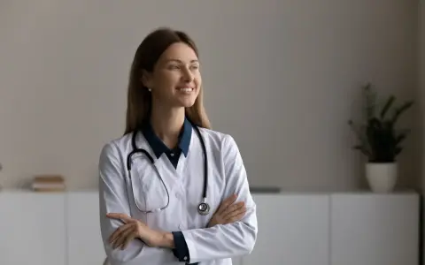 Une podologue souriante, avec un stéthoscope autour du cou, réfléchit à la rédaction d'une lettre pour le médecin traitant.