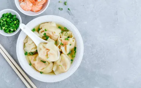 Aksamitna zupa wonton z krewetkami i szczypiorkiem, podana z pałeczkami.