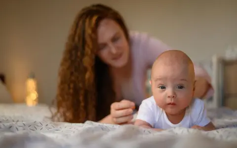 Maluch ćwiczy mięśnie szyi, kiedy układać noworodka na brzuchu. Mama czuwa z tyłu.
