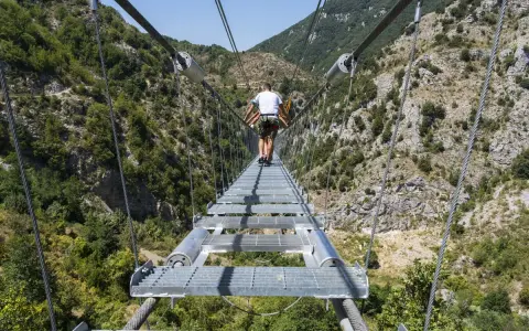 Un ponte tibetano in Puglia attraversa una gola verdeggiante, con persone che camminano su passerelle metalliche sospese tra montagne.