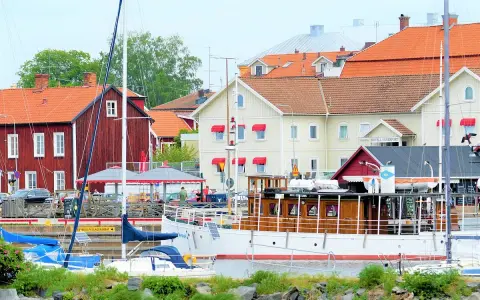 Båtar vid kajen framför hotell Vänerport i Mariestad. Röda och gula hus med tegeltak.