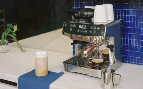 Un angolo caffè casa con macchina espresso, macinacaffè, tazzine e un bicchiere di cappuccino.