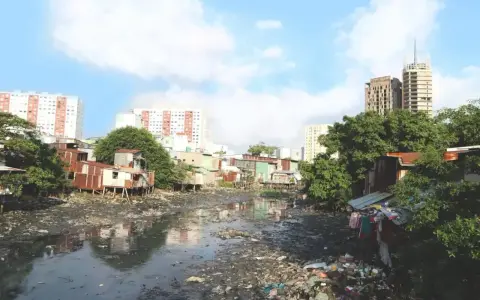 Un río lleno de basura y aguas residuales, rodeado de casas precarias y edificios modernos, ilustra los graves tipos de contaminación que afectan a esta comunidad.